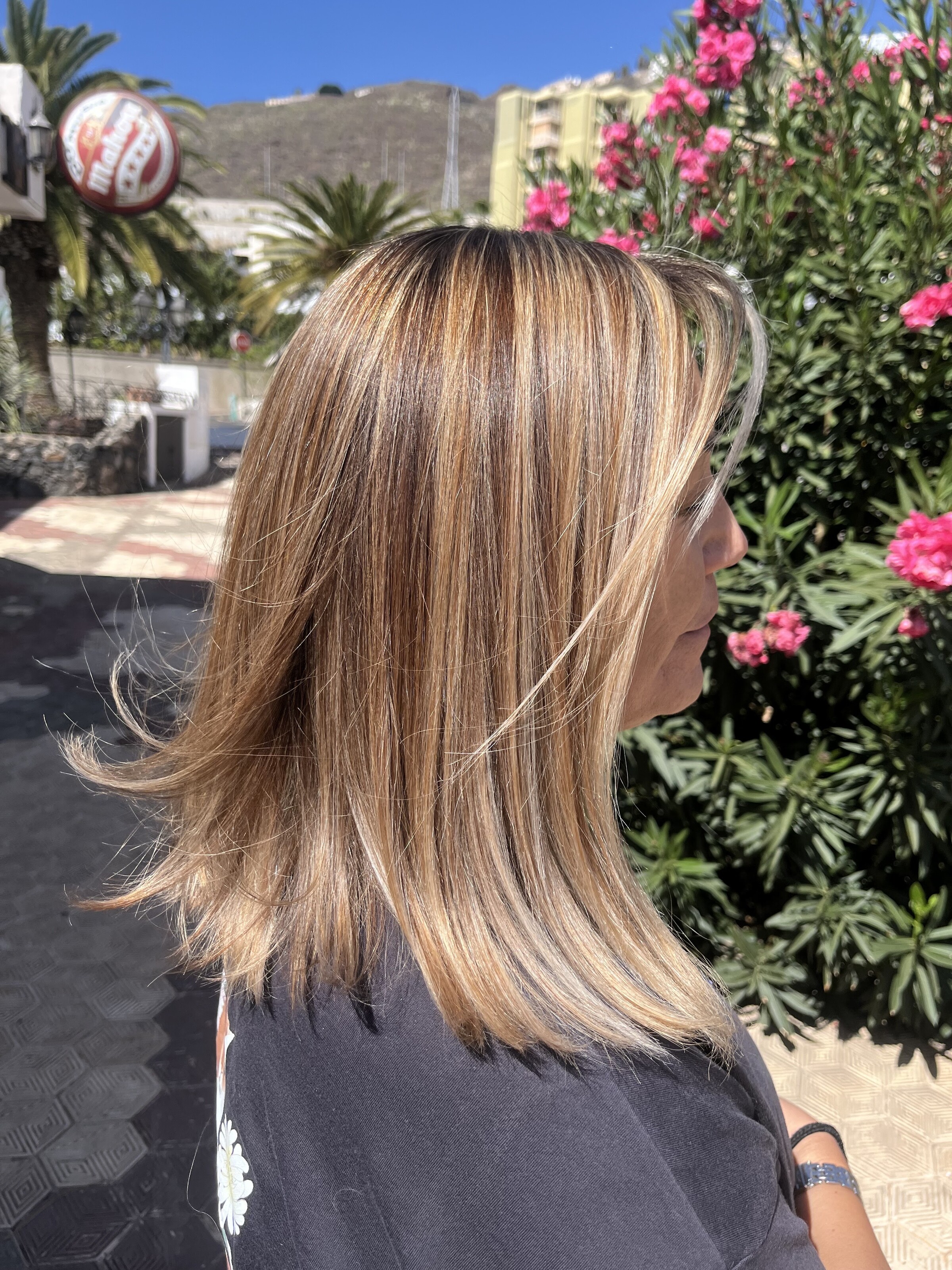 Melena con mechas balayage a la luz del día, junto a unas adelfas en flor